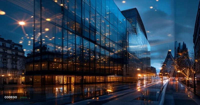 A cinematic editorial photograph of a modern European financial district at dusk, with the warm amber glow of street lamps co