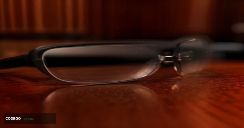 A dramatic close-up editorial photograph of a pair of sleek, modern smart glasses resting on a polished dark mahogany table, 