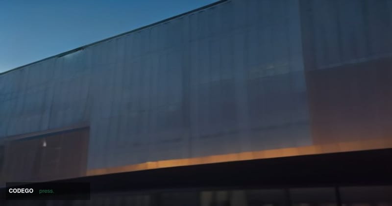 A cinematic editorial photograph shot from a low angle looking up at a sleek, modernist glass-and-steel corporate campus buil
